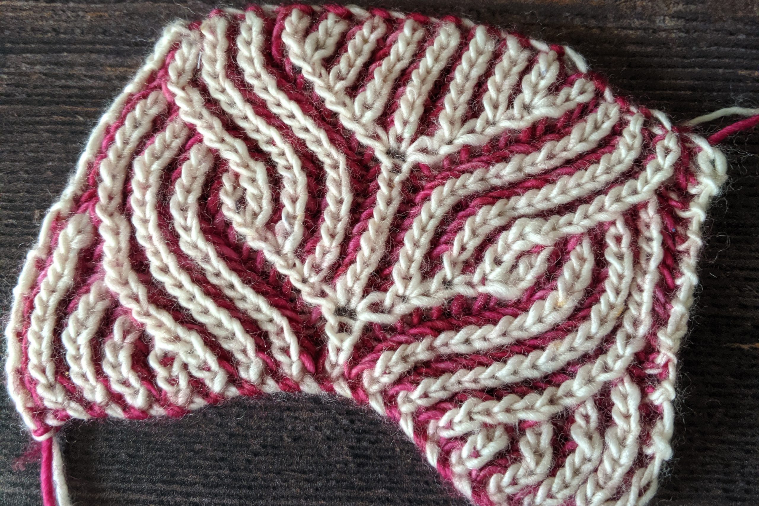 A piece of brioche knitting in pink and white yarn. The pattern resembles an owl.