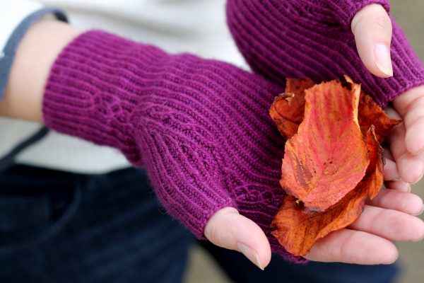 Twisted rib fingerless mitts with a narrow cable pattern that splits around the thumb (the model is holding bright autumn leaves)