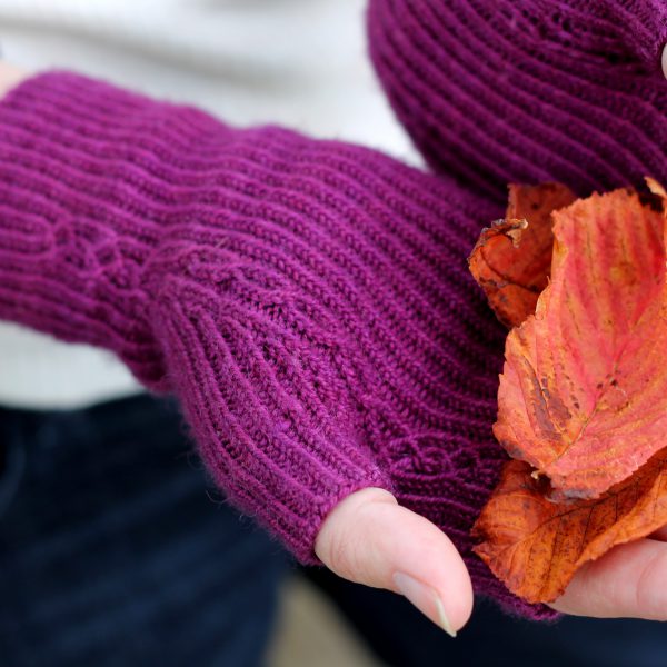 Twisted rib fingerless mitts with a narrow cable pattern that splits around the thumb (the model is holding bright autumn leaves)