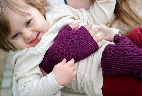 Twisted rib fingerless mitts with a large cable up the back of the hand and a narrow cable pattern that splits around the thumb (the model is holding a little girl)