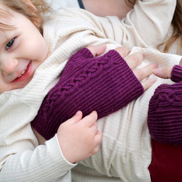 Twisted rib fingerless mitts with a large cable up the back of the hand and a narrow cable pattern that splits around the thumb (the model is holding a little girl)