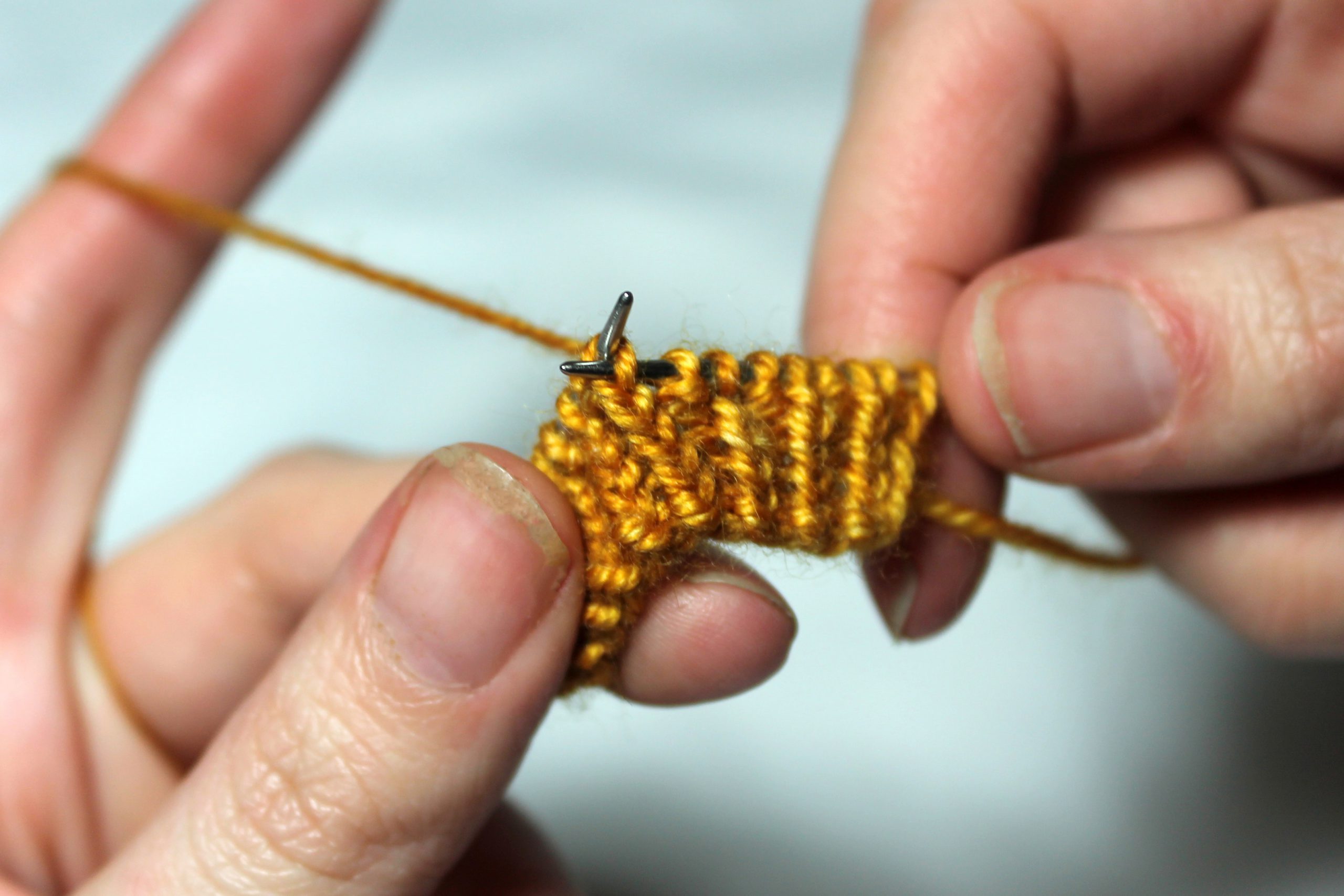 The right-hand needle has been inserted between the legs of the first stitch on the left-hand needle, from the back of the knitting