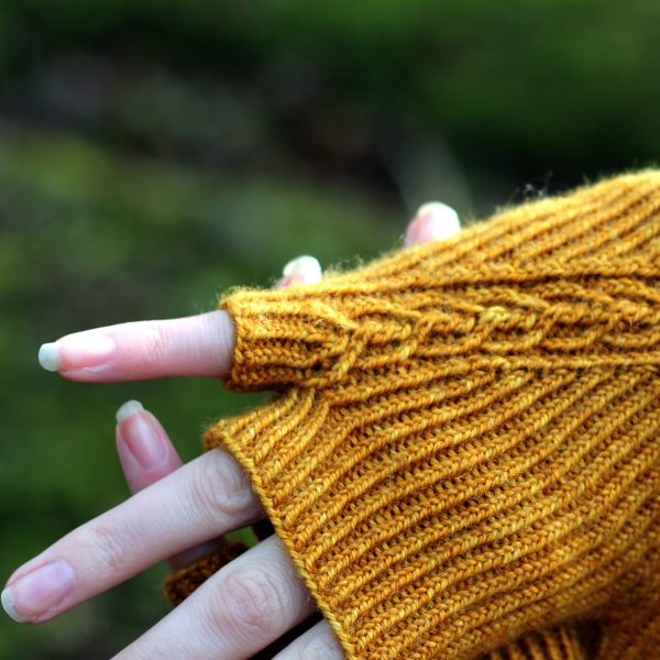 Twisted rib fingerless mitts with a narrow cable crossing the back of the hand from the inside of the wrist to the little finger. The little finger has a separate opening. A close up of the little finger detail