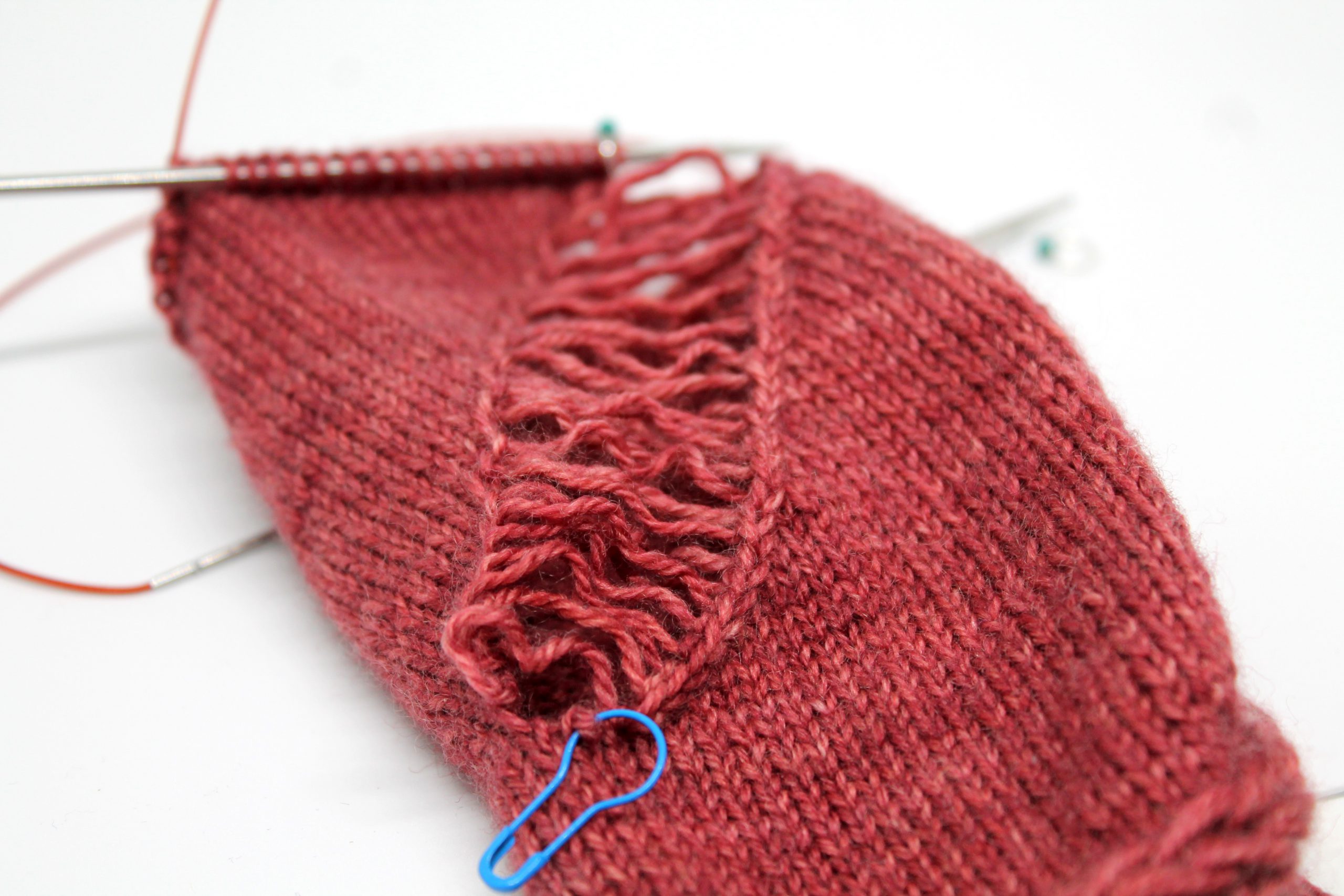 A piece of knitting with a wide laddered gap where stitches have been dropped. At the bottom of the photo is a stitch with a bulb stitch marker through it.