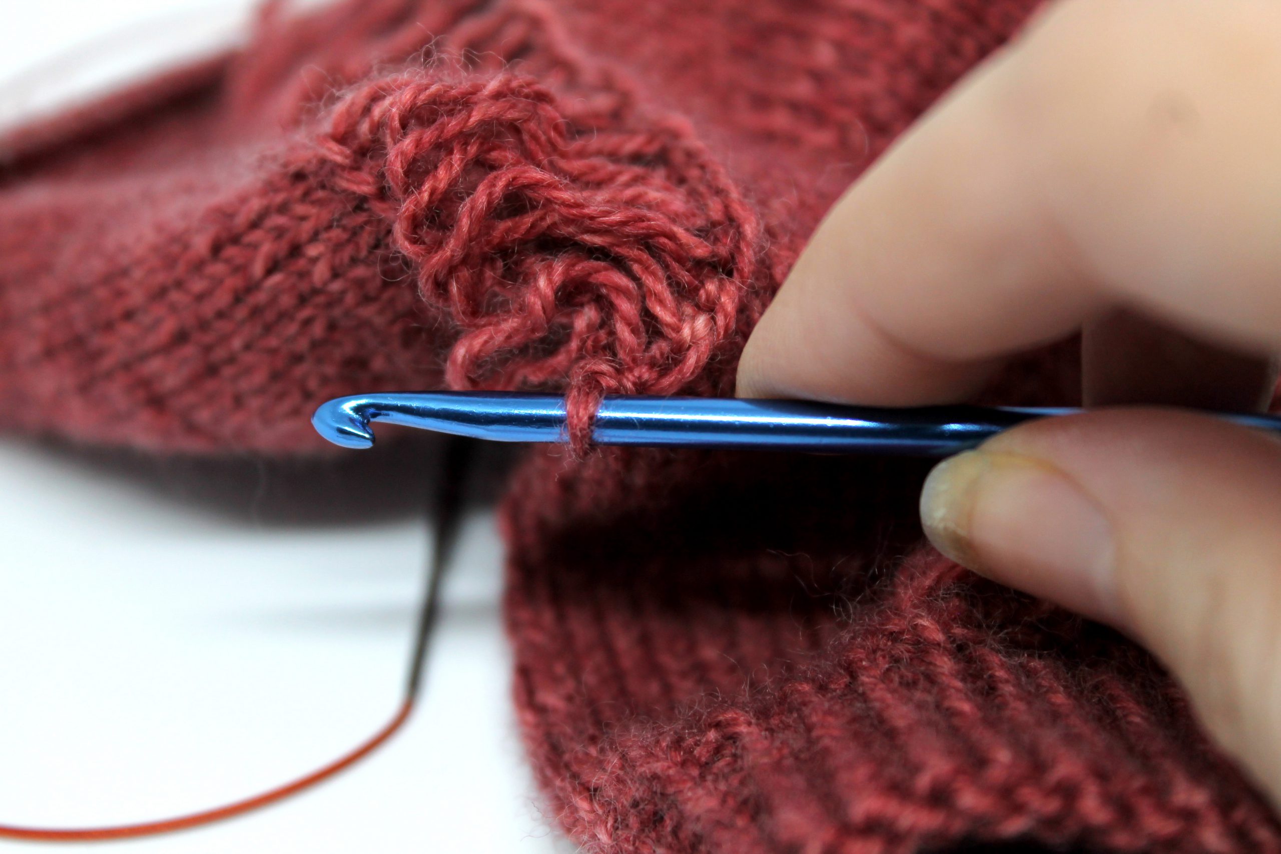 The stitch with the removable marker has now been place on a crochet hook, and the stitch marker removed. The laddered dropped stitches can still be seen at the back of the photo