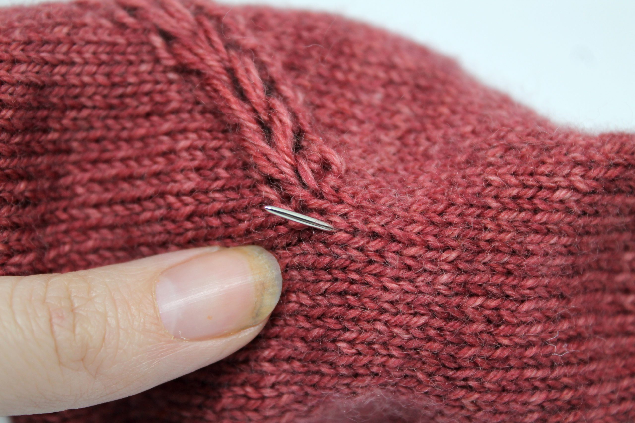 A tapestry needle sticking out of the fabric of a fingerless mitt ready to make the first chain stitch