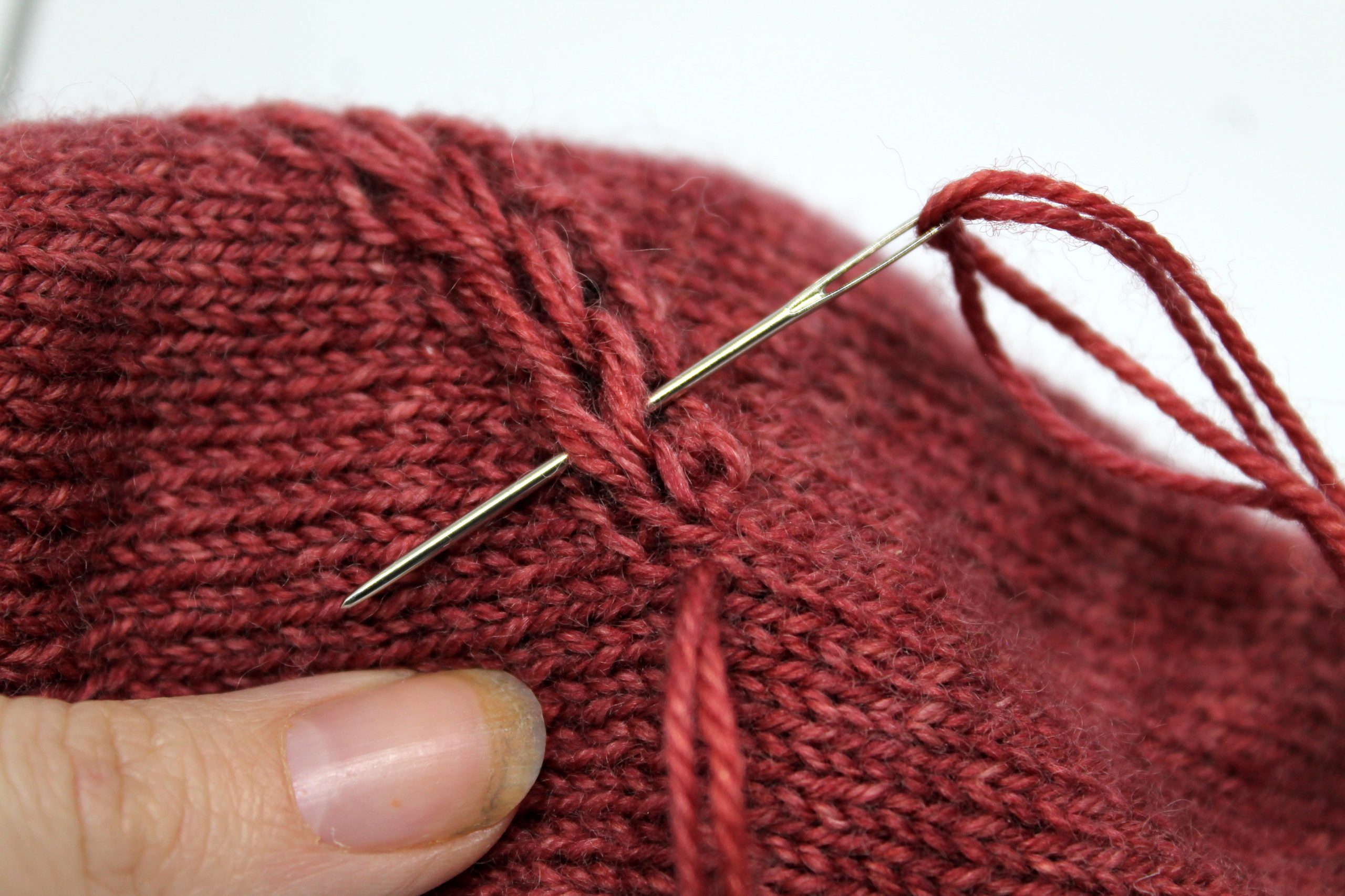 The tapestry needle passing behind the first stitch of the drop stitch braid