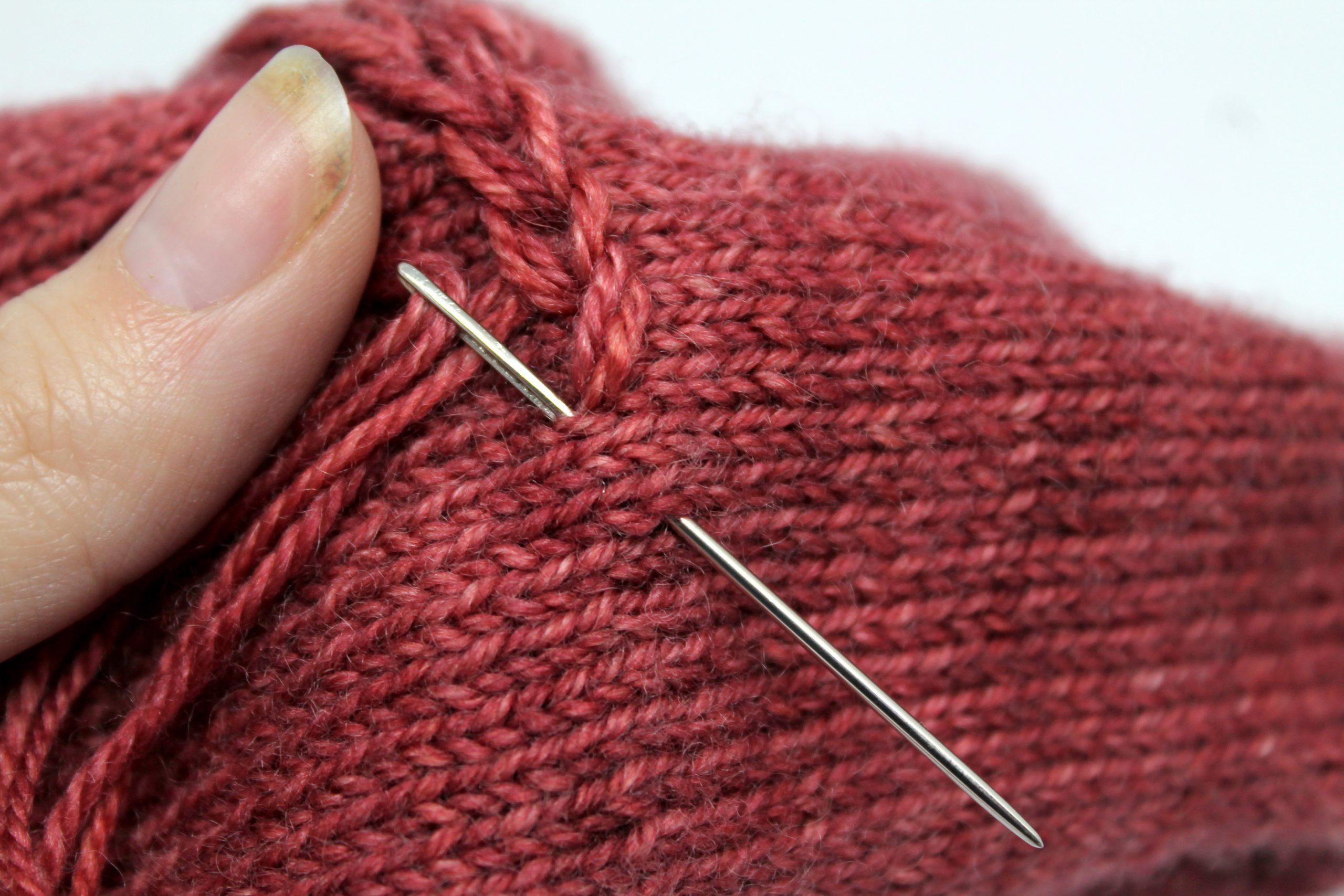 A tapestry needle entering and exiting the fabric of the mitt to finish one chain stitch and start the next