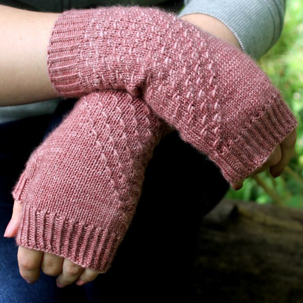 Fingerless mitts knit in pink yarn with a textured pattern travelling diagonally across the back of each hand.