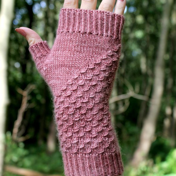 A fingerless mitt knit in pink yarn with a textured pattern travelling diagonally across the back of the hand.