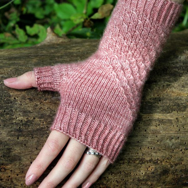 A fingerless mitt knit in pink yarn with a textured pattern travelling diagonally across the back of the hand.