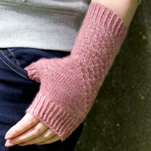 A fingerless mitt knit in pink yarn with a textured pattern travelling diagonally across the back of the hand.