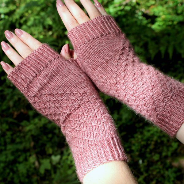 Fingerless mitts knit in pink yarn with a textured pattern travelling diagonally across the back of each hand.