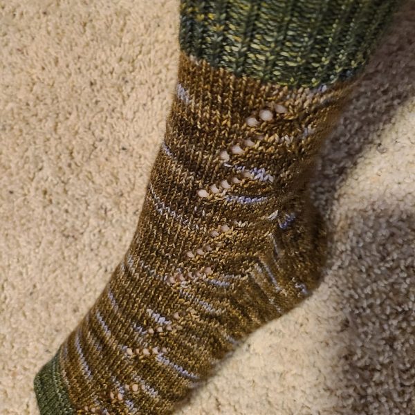 A modelled Giuthas sock knit in brown speckled yarn with contrast toe and cuff in green yarn on a sock blocker