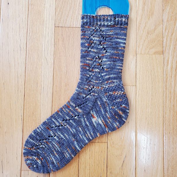 A Giuthas sock knit in blue speckled yarn on a sock blocker