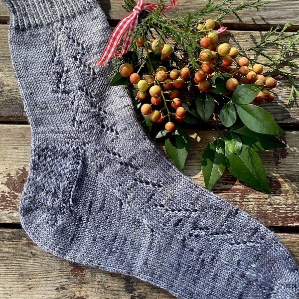 A giuthas sock knit in blue grey yarn with winter leaves and berries