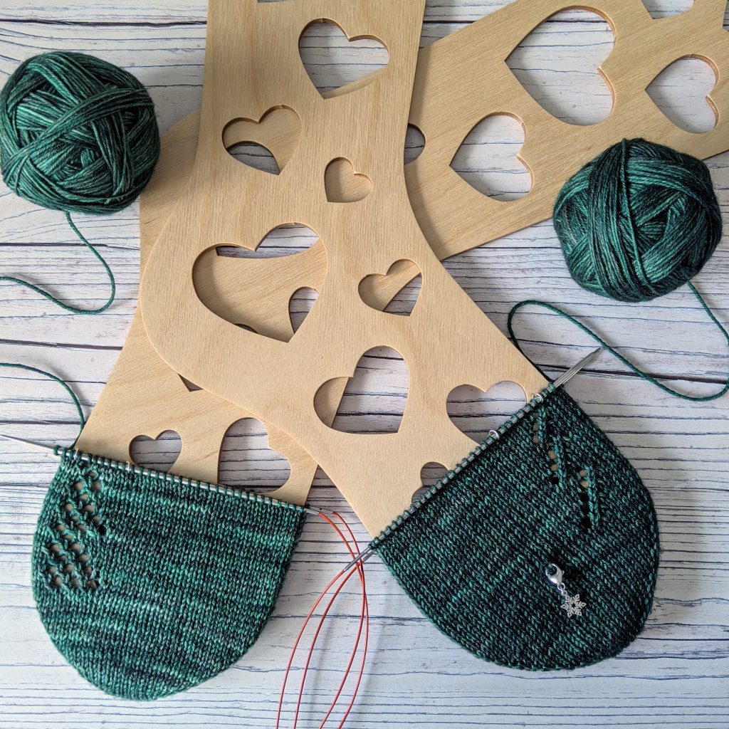 Two sock toes. the left has a fir tree knit in a lace mesh pattern, the one on the right just has the fir tree shape outlined in lace.