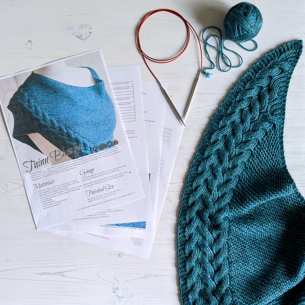 A knitting pattern with a ball of yarn, knitting needles and part of the shawl made form the pattern