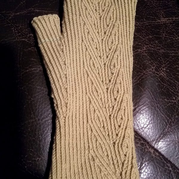 A light coloured fingerless mitt with twisted rib and a faux cable pattern, against a dark leather background