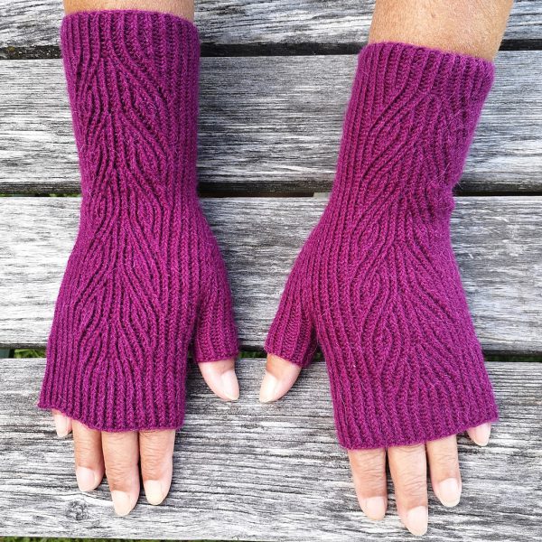 A pair of purple fingerless mitts with twisted rib and a faux cable pattern, against a grey wooden background