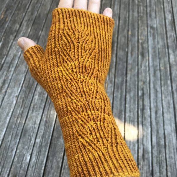 A golden fingerless mitt with twisted rib and a faux cable pattern, against a wooden background