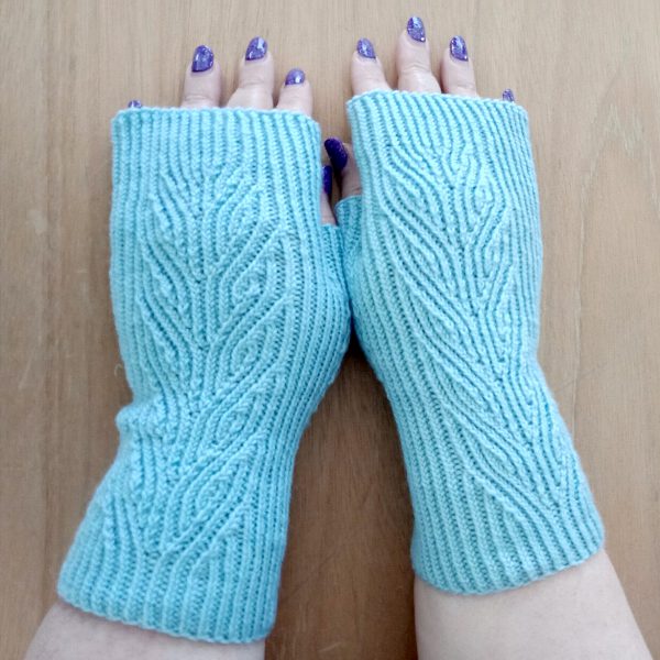 A pair of light blue fingerless mitts with twisted rib and a faux cable pattern, against a wooden background