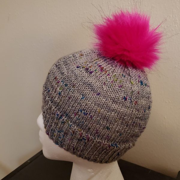 A grey hat with colourful speckles and a pink faux fur pompom on a foam head