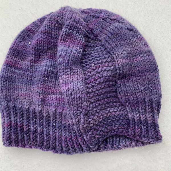 A hat knit in shades of purple with two garter stitch columns laid flat