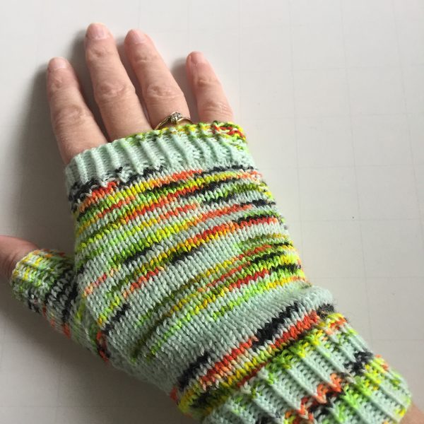 A hand wearing a fingerless mitt knit in variegated yarn