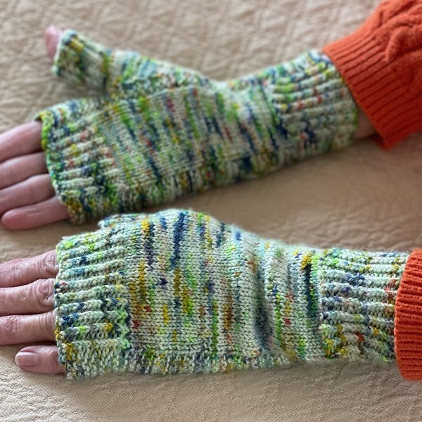 Two hands wearing a pair fingerless mitts knit in variegated yarn with colourful strips showing the garter stitch columns around the thumb gusset and the outside of the hand