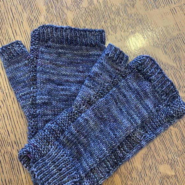 A pair of fingerless mitts knit in blue yarn showing the garter stitch columns around the thumb gusset and the outside of the hand
