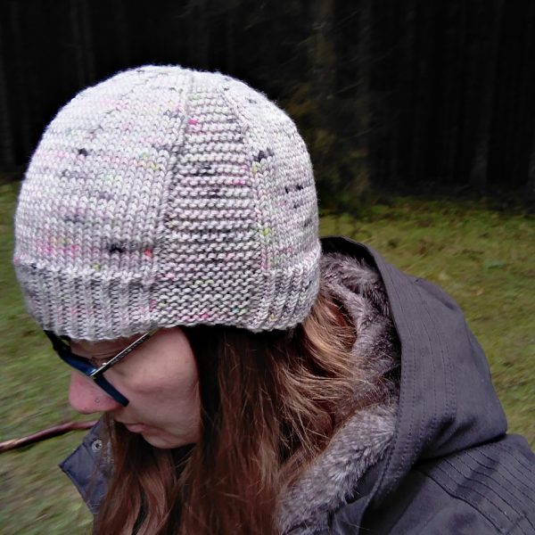 A woman wearing a beanie hat knit in grey yarn with colourful speckles and garter stitch columns up each side