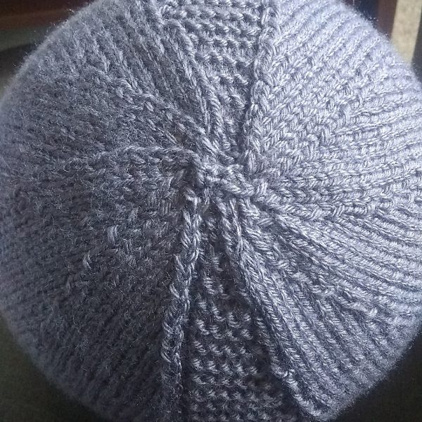 The crown of a beanie hat knit in grey yarn with garter stitch columns up each side