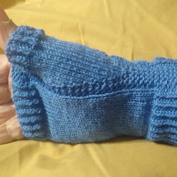 A hand wearing a fingerless mitt knit in blue yarn with colourful strips showing the garter stitch columns around the thumb gusset and the outside of the hand