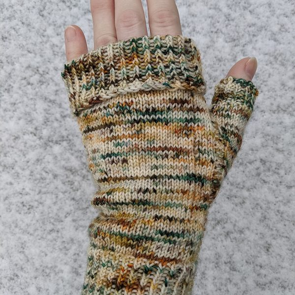 A hand wearing a fingerless mitt knit in variegated yarn showing the garter stitch columns around the thumb gusset and the outside of the hand and a folded down cuff