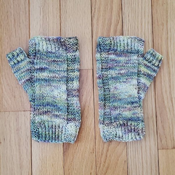 A pair of fingerless mitts knit in pastel yarn showing the garter stitch columns around the thumb gusset and the outside of the hand