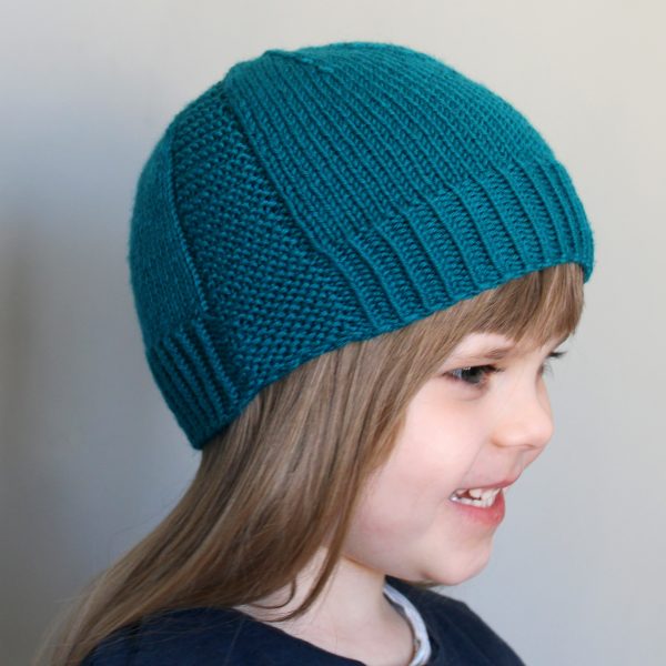 A young girl wearing a beanie hat knit in teal yarn with garter stitch columns up each side