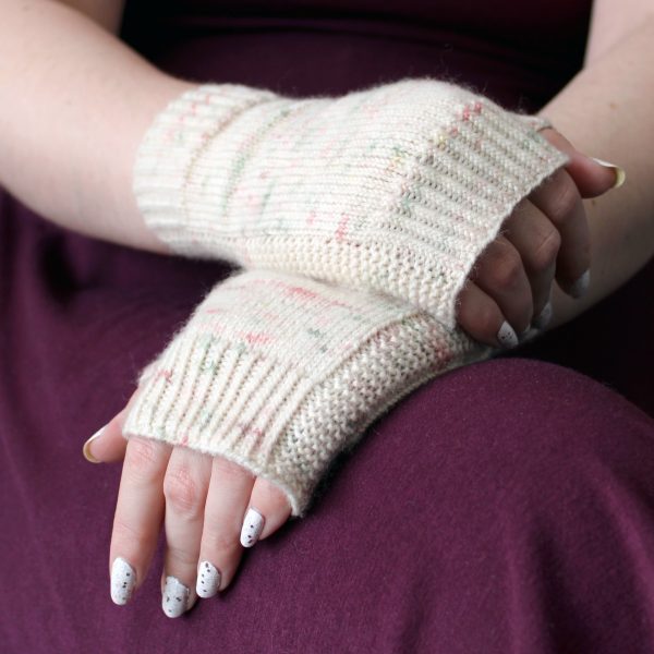 Two hands clasped showing the garter stitch columns around the outside of the hand of a pair of fingerless mitts knit in cream yarn with pink and green speckles