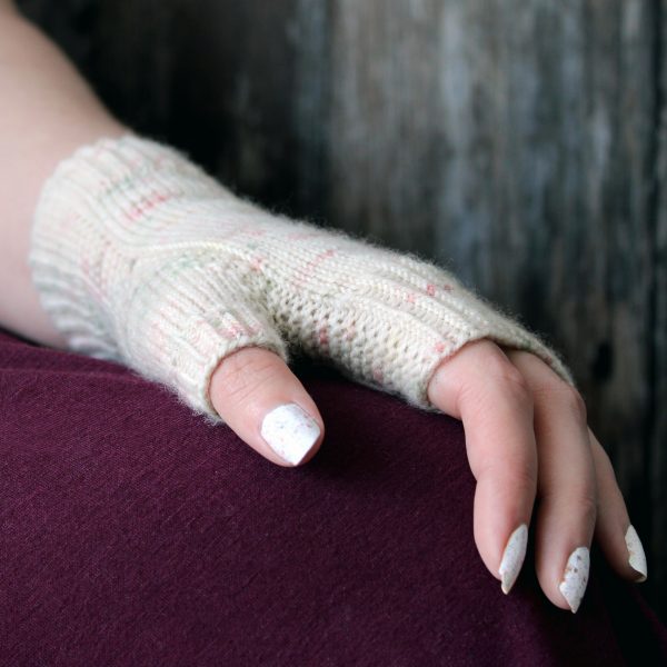 A hand showing the garter stitch column wrapping around the thumb gusset of a fingerless mitt knit in cream yarn with pink and green speckles