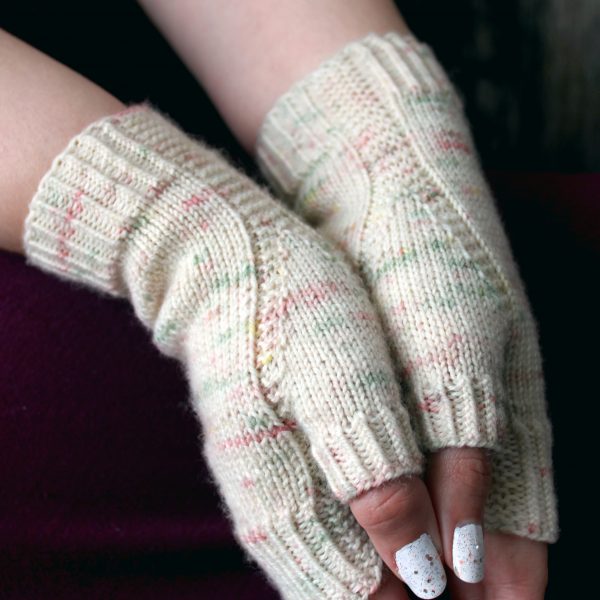 Two hands pressed together showing the garter stitch columns wrapping around the thumb gussets of a pair of fingerless mitts knit in cream yarn with pink and green speckles