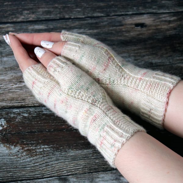 Two hands pressed together showing the garter stitch columns wrapping around the thumb gussets of a pair of fingerless mitts knit in cream yarn with pink and green speckles