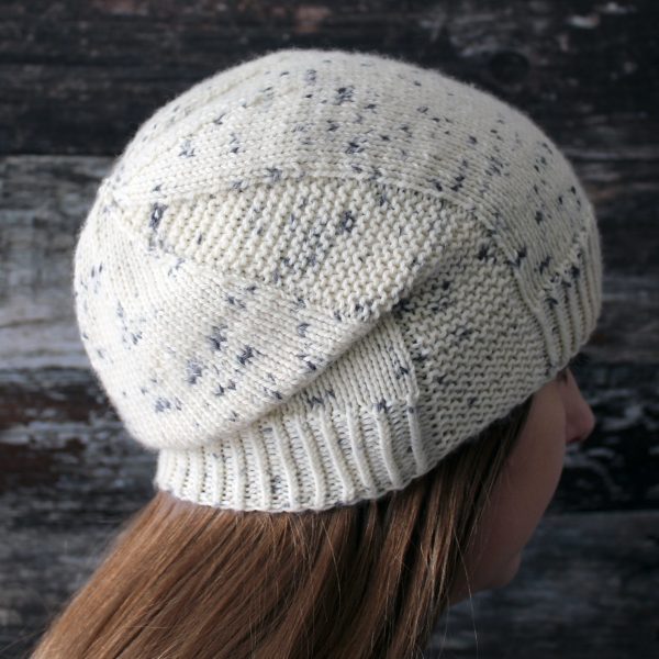 A woman wearing a slouchy hat knit in white yarn with black speckles and garter stitch columns up each side