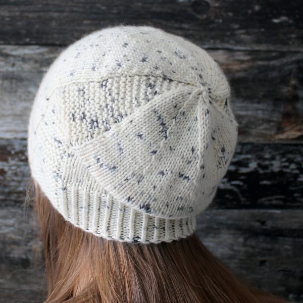 A woman wearing a slouchy hat knit in white yarn with black speckles and garter stitch columns up each side