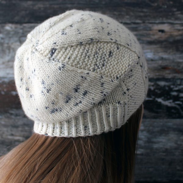 A woman wearing a slouchy hat knit in white yarn with black speckles and garter stitch columns up each side