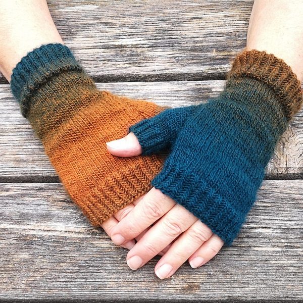 Two hands wearing a pair fingerless mitts knit in gradiented yarn with colourful strips showing the garter stitch columns around the thumb gusset and the outside of the hand