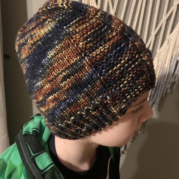 A boy wearing a beanie hat knit in variegated yarn with garter stitch columns up each side