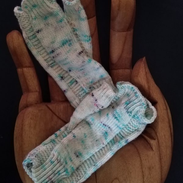 A pair of fingerless mitts knit in white speckled yarn showing the garter stitch columns around the thumb gusset and the outside of the hand