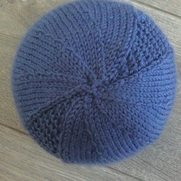 The crown of a beanie hat knit in blue yarn with garter stitch columns up each side