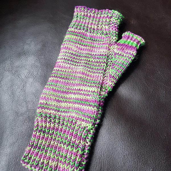 A fingerless mitt knit in purple and green yarn showing the garter stitch columns around the thumb gusset and the outside of the hand