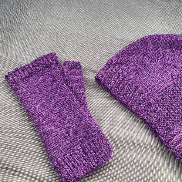 A fingerless mitt knit in purple yarn showing the garter stitch columns around the thumb gusset and the outside of the hand